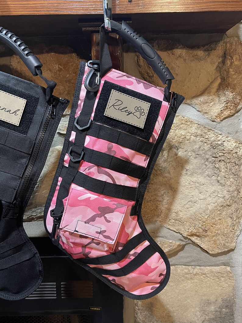 May include: Pink and black camouflage stocking with a black handle and a brown patch that says "Riley" with a paw print.
