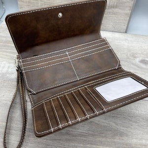 May include: A brown leather wallet with a wrist strap and white stitching. The wallet has multiple card slots and a clear ID window.