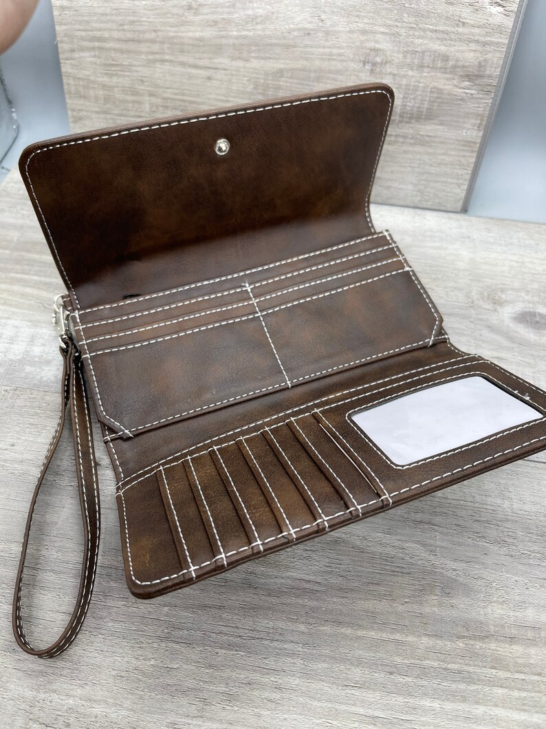 May include: A brown leather wallet with a wrist strap and white stitching. The wallet has multiple card slots and a clear ID window.