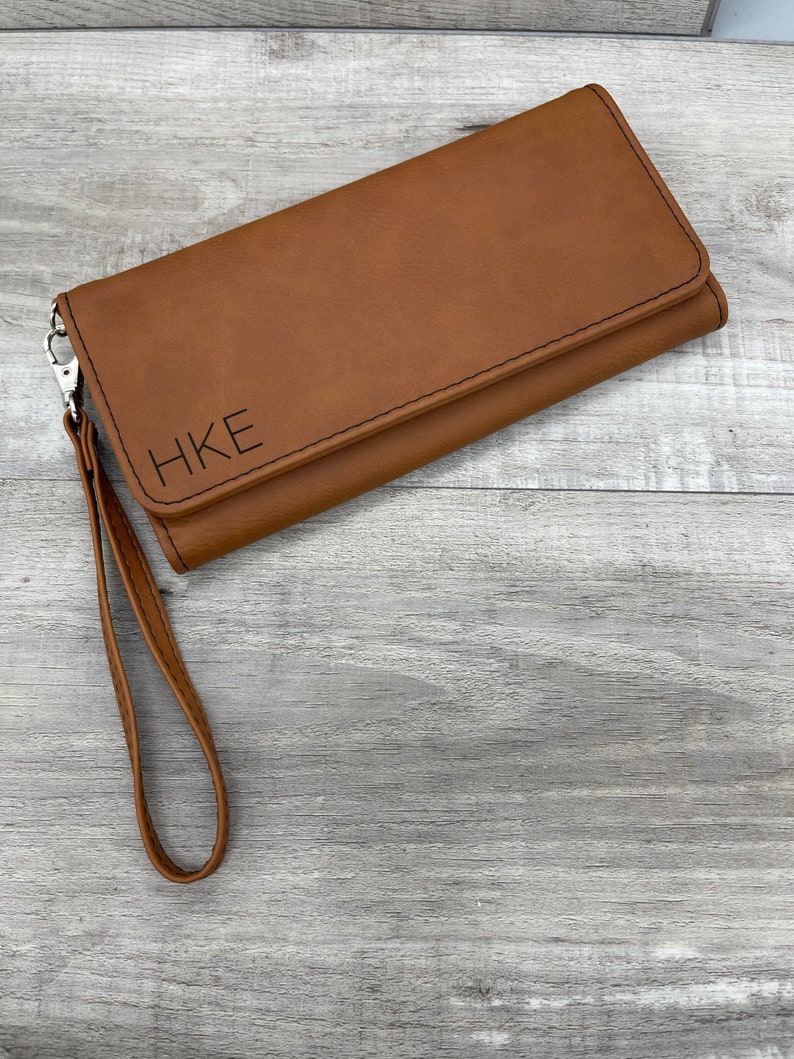 May include: A brown leather wallet with a wrist strap and the initials "HKE" embossed on the front.