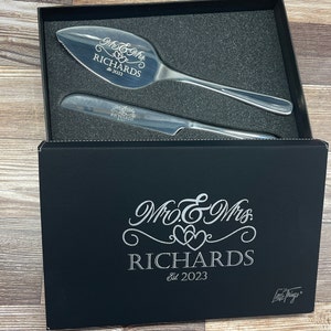 May include: A black gift box with a silver engraved design that says "Mr. & Mrs. Richards Est. 2023" and a silver cake knife and server set inside.
