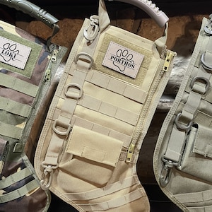May include: Tan-colored, tactical-style dog stocking with a zipper, multiple pockets, and a loop handle. The stocking has a personalized patch with the name "PORTHOS" and a paw print.