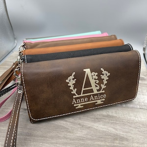 May include: A stack of brown leather wallets with a personalized monogram. The top wallet has the letter "A" with a floral design and the name "Anne Anice" engraved on it.