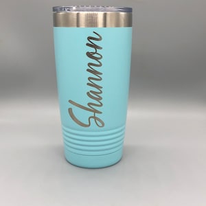 May include: A light blue stainless steel tumbler with a silver lid and the name "Shannon" engraved on the side.