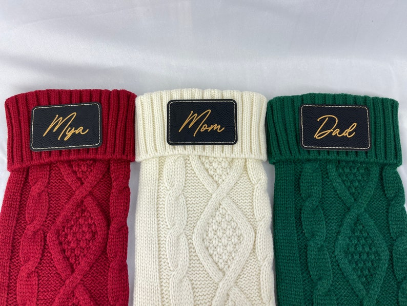 May include: Three knitted Christmas stockings with personalized names. The stockings are red, white, and green. The names are "Mya", "Mom", and "Dad" in gold lettering.