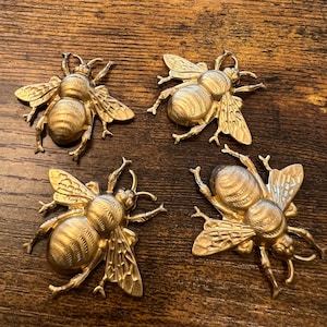 Peut inclure: Quatre figurines d'abeilles en métal de couleur dorée. Les abeilles ont des ailes et des corps détaillés.