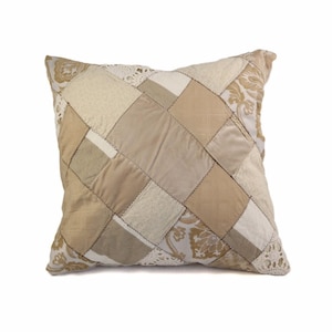 May include: A beige and white patchwork cushion with a diamond pattern. The cushion is made of different fabrics and textures.