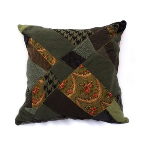 May include: A square patchwork cushion with a green, brown, and black colour scheme. The cushion is made of different fabrics, including velvet, floral print, and houndstooth.