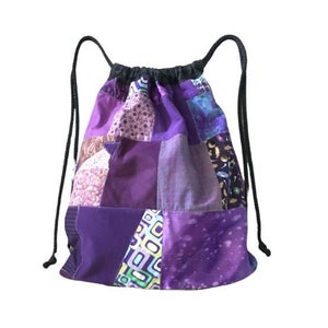 Op de afbeelding: Paarse patchwork trekkoordtas met zwarte trekkoorden. De tas is gemaakt van verschillende tinten paarse stof met verschillende patronen.