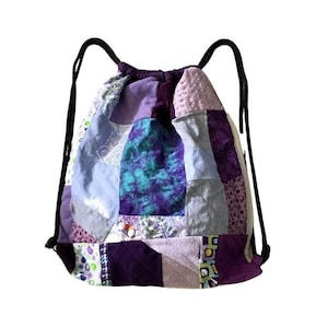 Op de afbeelding: Paarse, blauwe en witte patchwork trekkoordtas met zwarte trekkoorden.