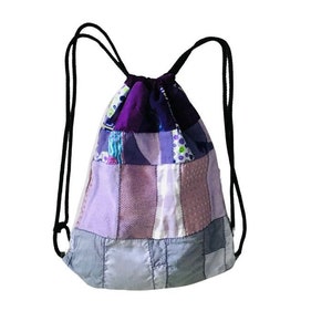 Peut inclure: Un sac à dos à cordon de serrage en patchwork violet et gris avec des cordons noirs.