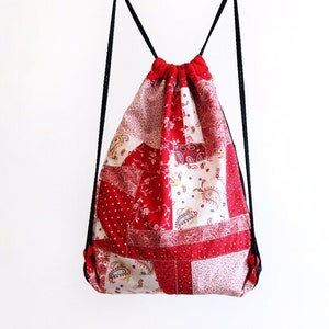 Könnte beinhalten: Rote und weiße Patchwork-Kordeltasche mit schwarzen Kordeln. Die Tasche besteht aus verschiedenen Stoffen mit Blumen- und Paisley-Mustern.