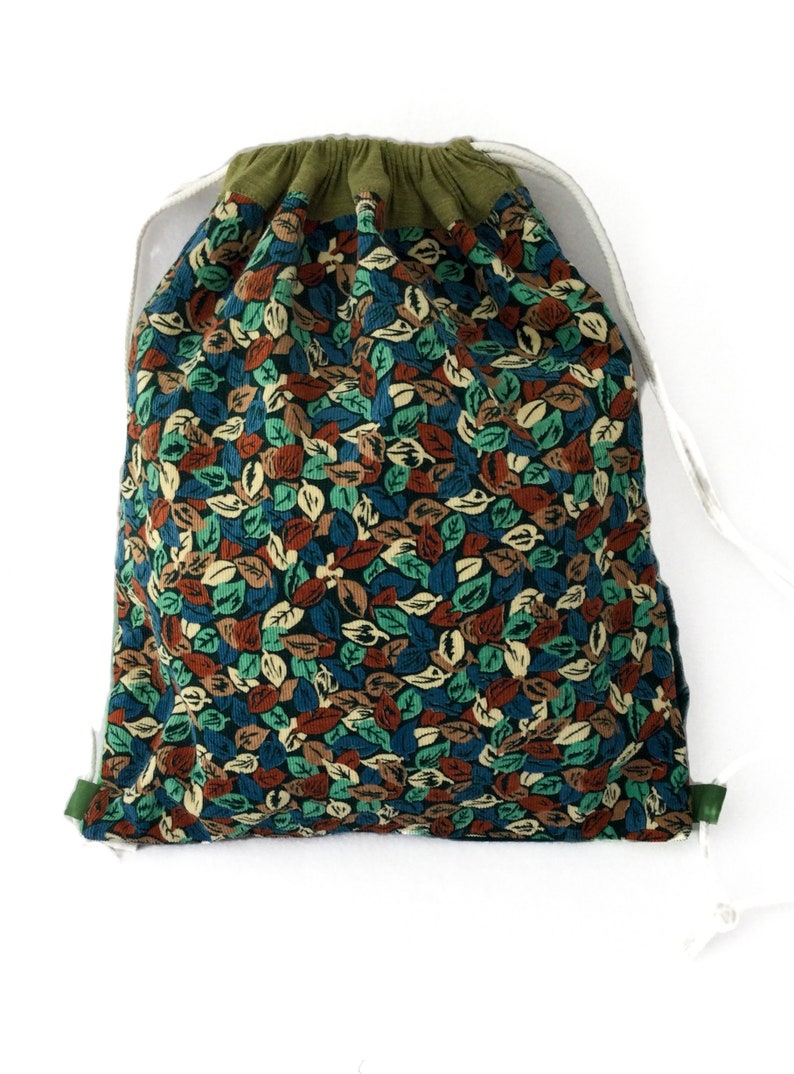 May include: A green drawstring bag with a leaf print pattern in shades of blue, green, brown, and cream. The bag is made of a soft, textured fabric.