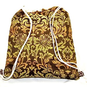 Op de afbeelding: Een bruine trekkoordtas met een gouden en groene bloemenprint. De tas heeft witte trekkoorden.