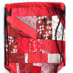 May include: Red drawstring bag made from patchwork fabric with a variety of red, white, and black patterns.