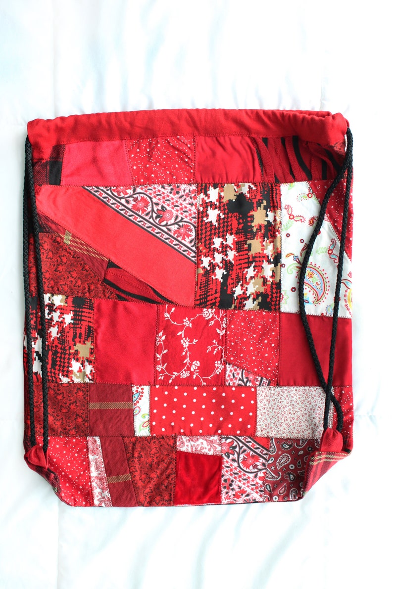 May include: Red drawstring bag made from patchwork fabric with a variety of red, white, and black patterns.