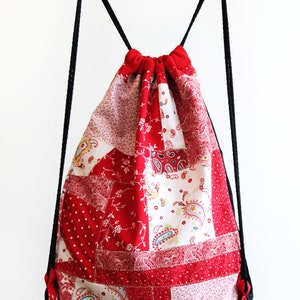 May include: Red and white patchwork drawstring bag with black drawstrings. The bag is made of different fabrics with floral and paisley patterns.