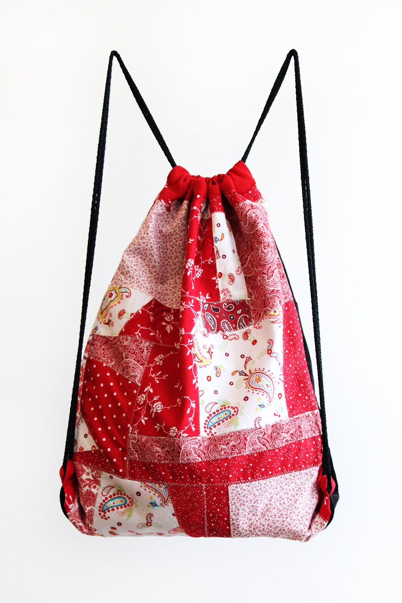 May include: Red and white patchwork drawstring bag with black drawstrings. The bag is made of different fabrics with floral and paisley patterns.