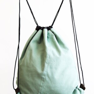 May include: A light green drawstring bag with black drawstrings and black handles. The bag is made of a soft, canvas-like material.