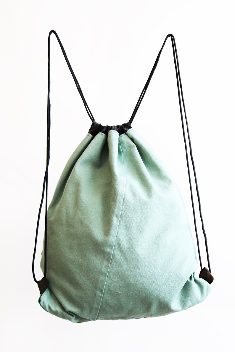 May include: A light green drawstring bag with black drawstrings and black handles. The bag is made of a soft, canvas-like material.