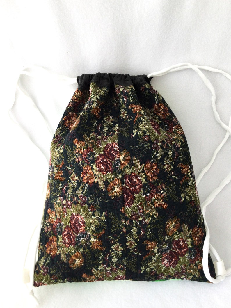 Puede incluir: Una bolsa de cord&oacute;n negro con un patr&oacute;n de tapicer&iacute;a floral en tonos rojos, verdes y dorados. La bolsa tiene cordones de color blanco.