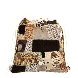 Peut inclure: Un sac à cordon en patchwork brun et beige avec un cordon blanc. Le sac est fait de différents tissus, dont du velours, du tweed et des tissus à motifs.