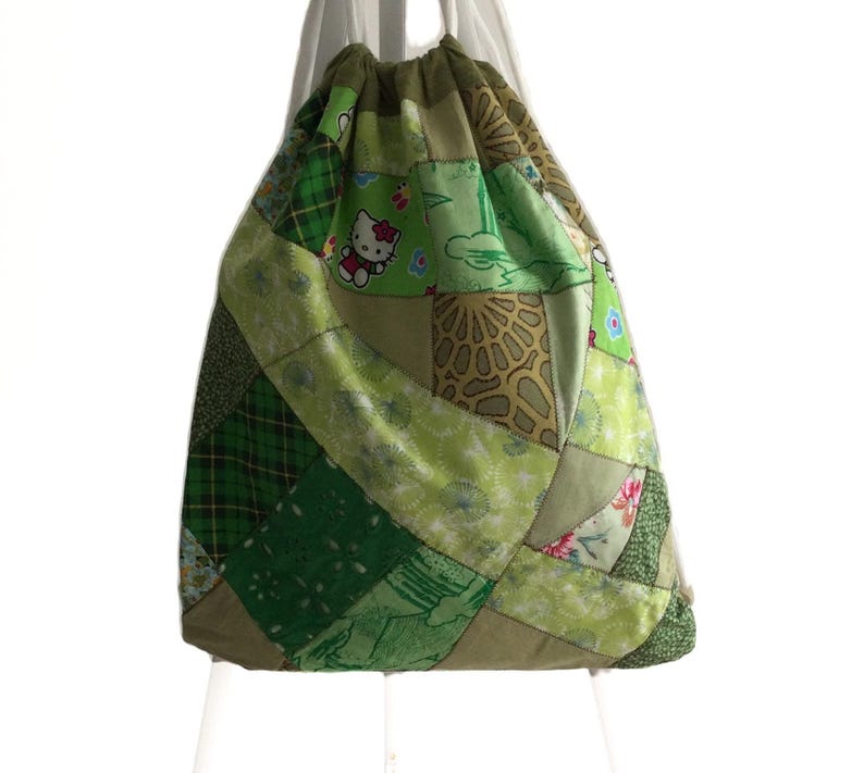 Op de afbeelding: Groene patchwork trekkoordtas met een Hello Kitty-ontwerp. De tas is gemaakt van verschillende groene stoffen met verschillende patronen.