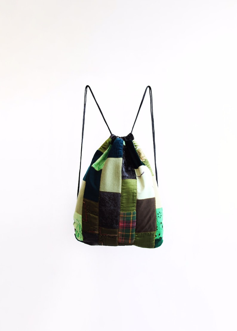 May include: A patchwork drawstring backpack in a green, brown and blue colour scheme. The bag is made from various fabrics and has a unique, handmade appearance.