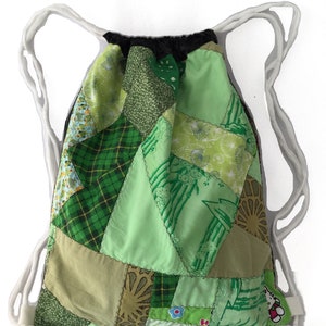 Puede incluir: Bolso de cord&oacute;n de patchwork verde con cordones blancos. El bolso est&aacute; hecho de varias telas verdes con diferentes patrones, incluyendo cuadros, flores y dise&ntilde;os geom&eacute;tricos.