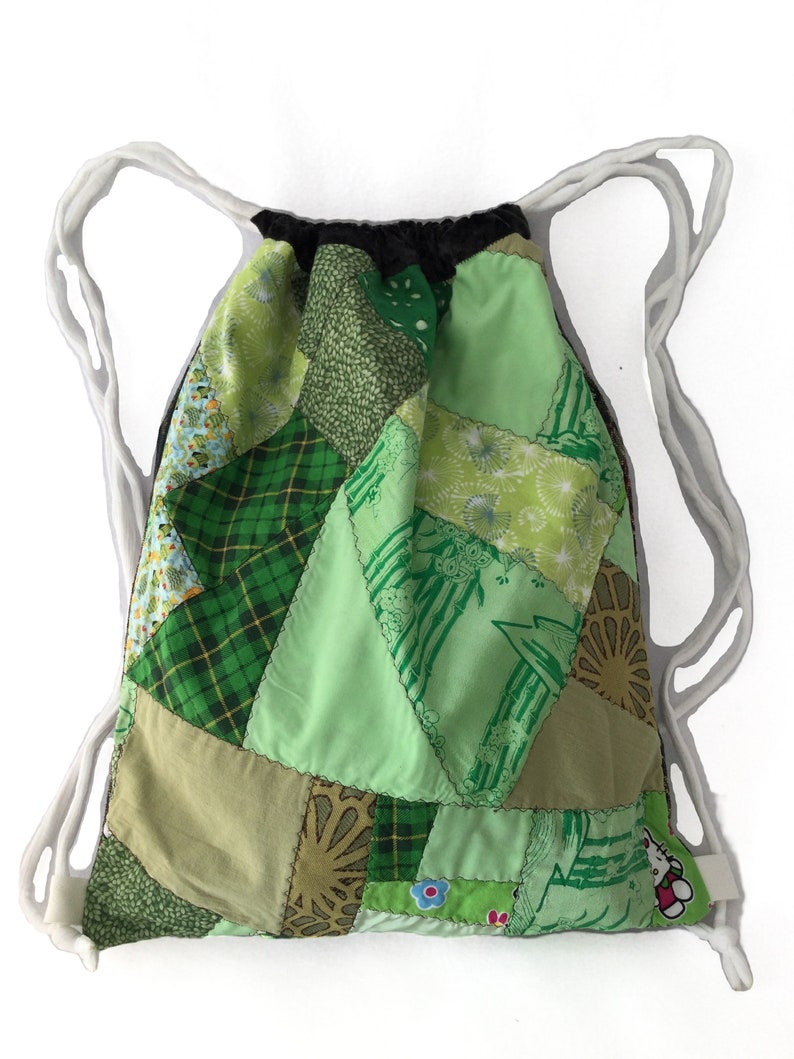 Puede incluir: Bolso de cord&oacute;n de patchwork verde con cordones blancos. El bolso est&aacute; hecho de varias telas verdes con diferentes patrones, incluyendo cuadros, flores y dise&ntilde;os geom&eacute;tricos.