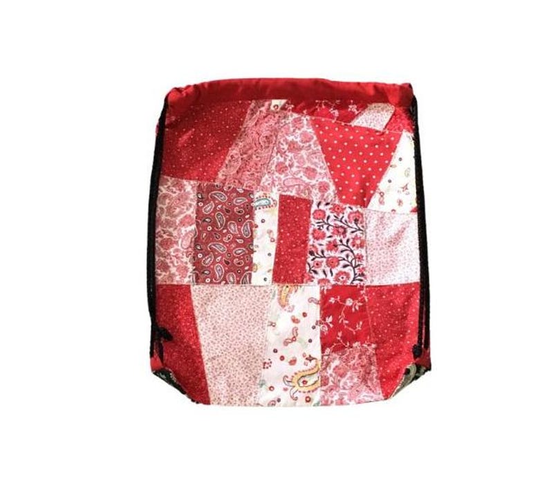 以下が含まれることがあります： 赤色の巾着袋で、パッチワークのデザインが施されています。様々な赤と白のフローラルパターンが特徴です。