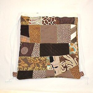 Op de afbeelding: Een bruine en witte patchwork trekkoordtas met verschillende patronen, waaronder dierenprint, bloemen en geometrische patronen.