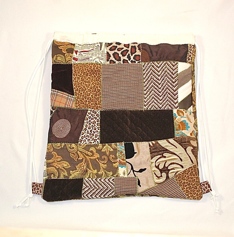 Op de afbeelding: Een bruine en witte patchwork trekkoordtas met verschillende patronen, waaronder dierenprint, bloemen en geometrische patronen.