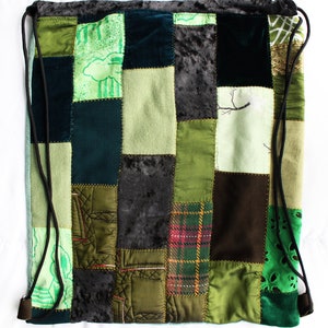 May include: A green, brown and black patchwork drawstring bag made from a variety of fabrics and textures. The bag features a mix of fabrics, including velvet, plaid and floral prints.