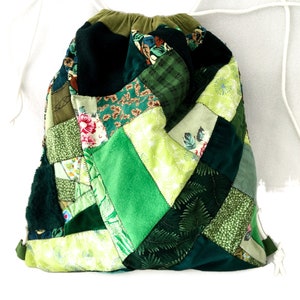 May include: A green patchwork drawstring bag made from different fabrics. The bag is made of various shades of green and has a white drawstring.