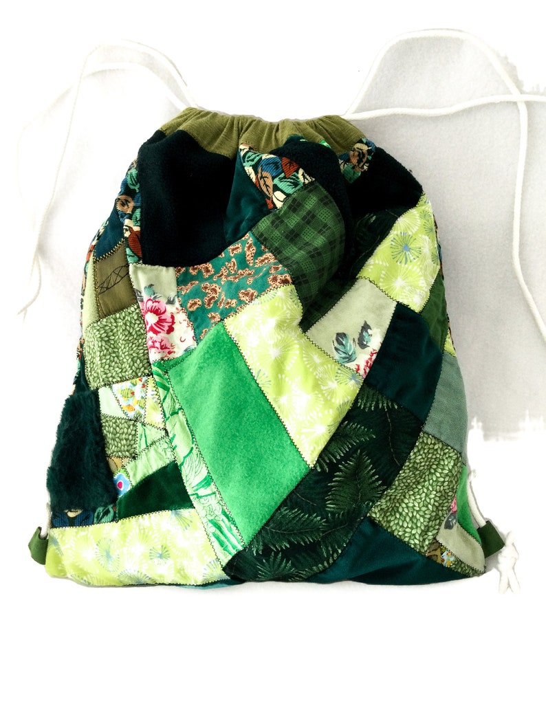 May include: A green patchwork drawstring bag made from different fabrics. The bag is made of various shades of green and has a white drawstring.