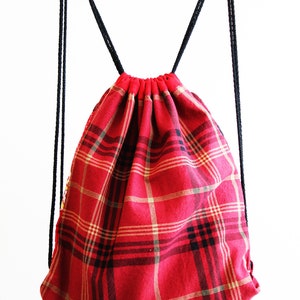 May include: Red and black plaid drawstring backpack with black drawstrings.