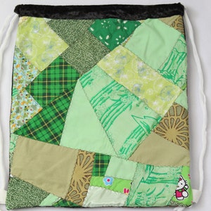 Puede incluir: Una bolsa de cord&oacute;n de retazos verde y marr&oacute;n con una parte superior de terciopelo negro. La bolsa est&aacute; hecha de varias telas con diferentes patrones, incluyendo cuadros verdes, flores verdes y blancas y marr&oacute;n con un dise&ntilde;o geom&eacute;trico. La bolsa tiene un cord&oacute;n blanco.