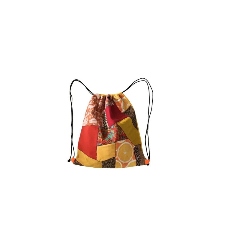 May include: A drawstring bag made of patchwork fabric in shades of red, yellow, and brown. The bag has a variety of patterns, including floral, geometric, and animal print.