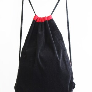 May include: Black drawstring bag with red trim. The bag is made of a soft, velvety material.