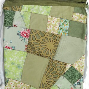 May include: A green patchwork drawstring bag with a variety of floral and geometric patterns. The bag is made of fabric scraps sewn together in a random pattern.