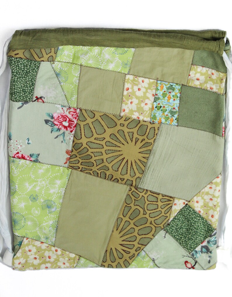 May include: A green patchwork drawstring bag with a variety of floral and geometric patterns. The bag is made of fabric scraps sewn together in a random pattern.
