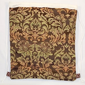 Op de afbeelding: Een bruine trekkoordtas met een witte voering en een bloemenpatroon. De tas heeft een bruin en wit trekkoord.