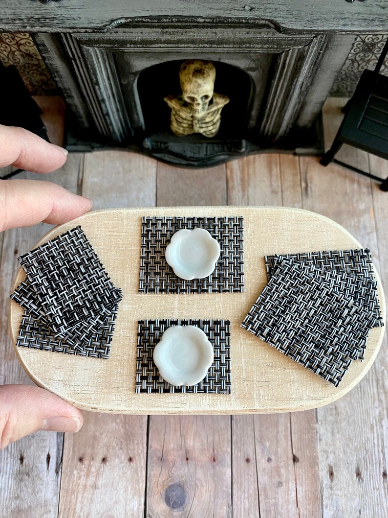 May include: A set of four black and white woven placemats with white ceramic plates on top. The placemats are on a wooden table.