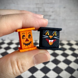 May include: Two miniature wooden Halloween decorations. One is a jack-o'-lantern with a carved face and the other is a black cat with white eyes and fangs.