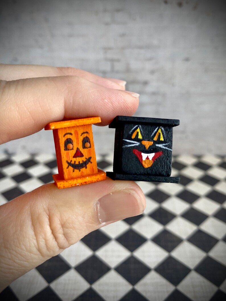 May include: Two miniature wooden Halloween decorations. One is a jack-o'-lantern with a carved face and the other is a black cat with white eyes and fangs.