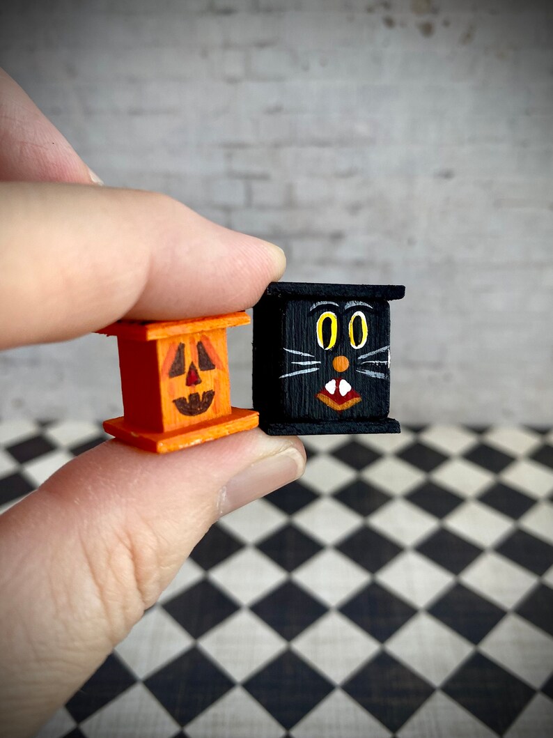 May include: Two small wooden Halloween decorations. One is a pumpkin with a carved face and the other is a black cat with yellow eyes and a white mouth.