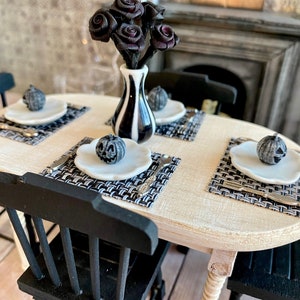 May include: A miniature dining table set with black chairs, white placemats, and black and white striped plates. A vase with black roses sits in the center of the table.