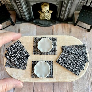 May include: Four black and white woven placemats with white ceramic plates on a wooden table.