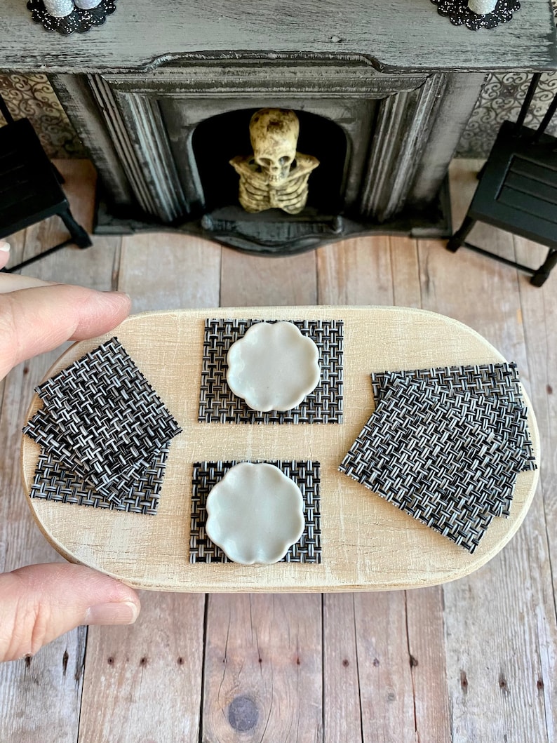 May include: Four black and white woven placemats with white ceramic plates on a wooden table.
